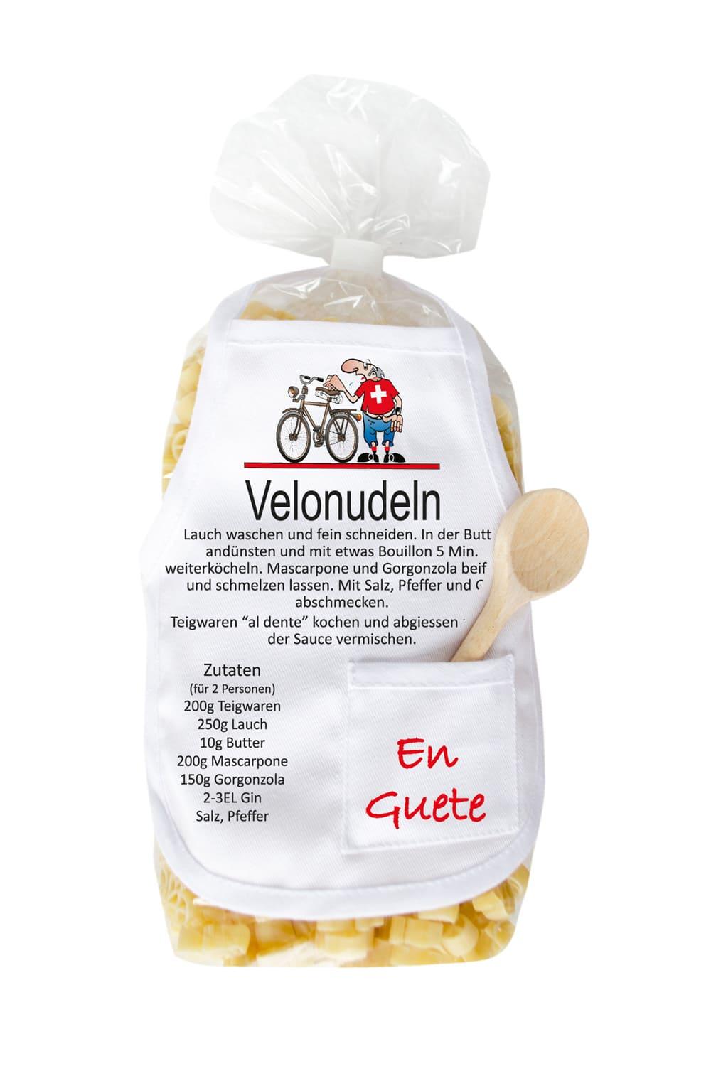 Die Fahrrad Pasta sind in einer Velo Form und in einer schoenen Verpackung mit Mini-Schuerze. Auf der laessigen Kochschuerze steht ein feines Rezept zum Nachkochen und die Aufschrift: Velonudeln. Zusaetzlich befindet sich in der kleinen Tasche, ein kleiner Kochloeffel aus Holz. Originelles Pastageschenk!
