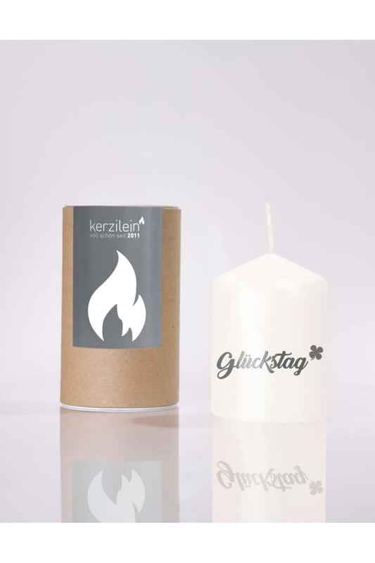 Flaemmchen von Kerzilein! Auf der Kerze befindet sich der Spruch: Glueckstag! Die Stumpenkerze ist weiss und verpackt in einer runden Kartonverpackung. 