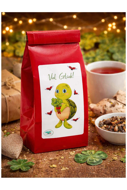 Spruch-Tee mit der Aufschrift: Viel Glueck, und der niedlichen Schildkroete Lia. Die Schildkroete haelt einen Strauss voller vierblaettrigen Kleeblaettern in der Hand. Glueckstee fuer jeden Anlass! 